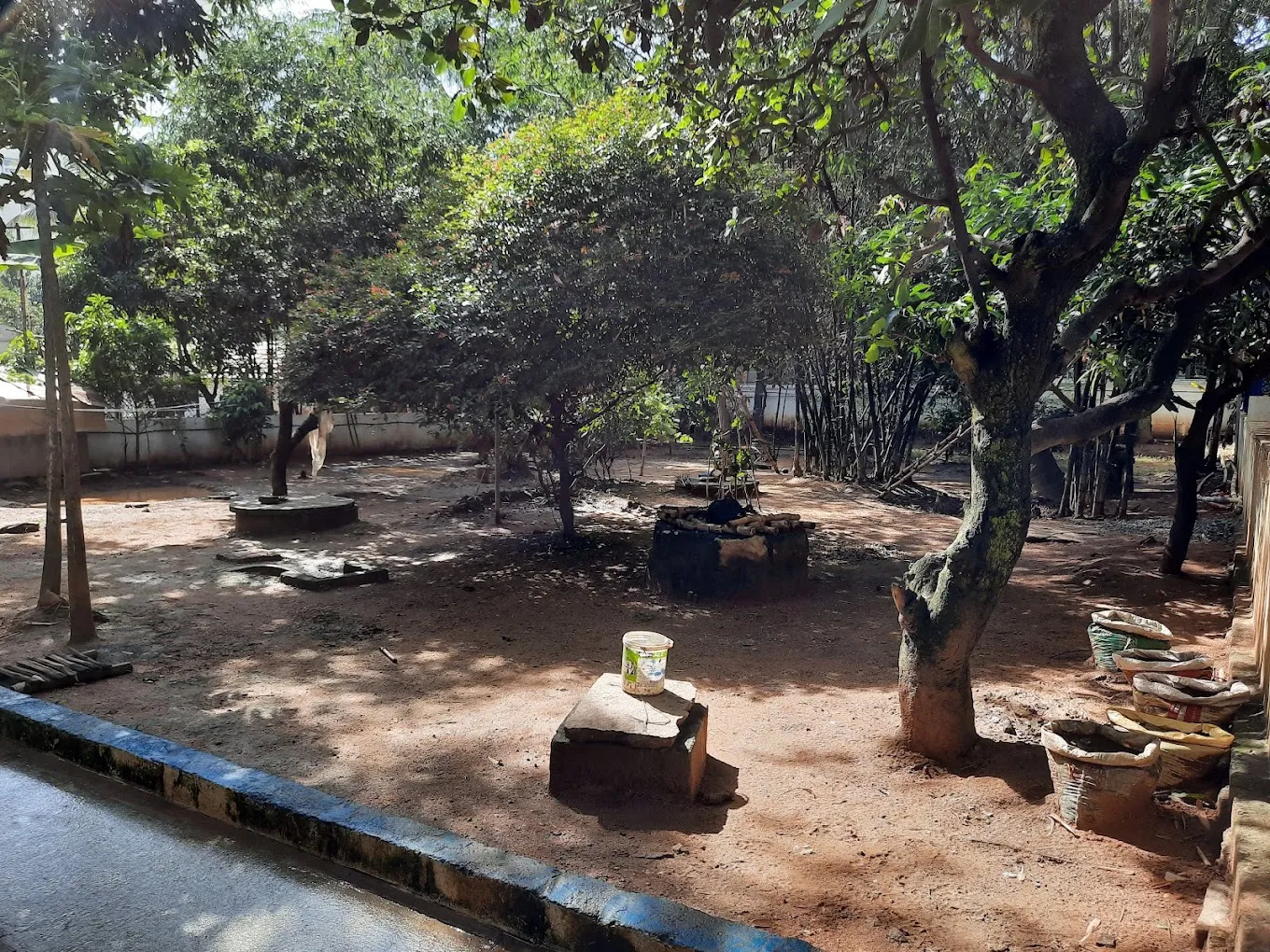 Tree-shaded dirt yard with stone blocks and sacks stacked at the edge