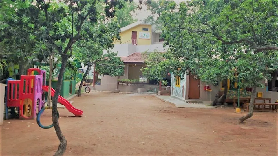 Colourful children's slide and tyre swing in a tree-shaded dirt play area