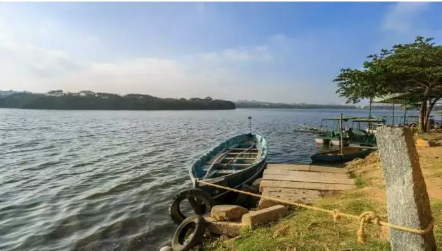 Two boats moored near a wooden dock on Madiwala Lake with hills beyond