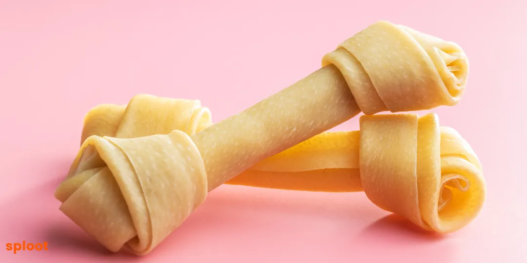 Two rolled rawhide bone-shaped chew treats on a pink background