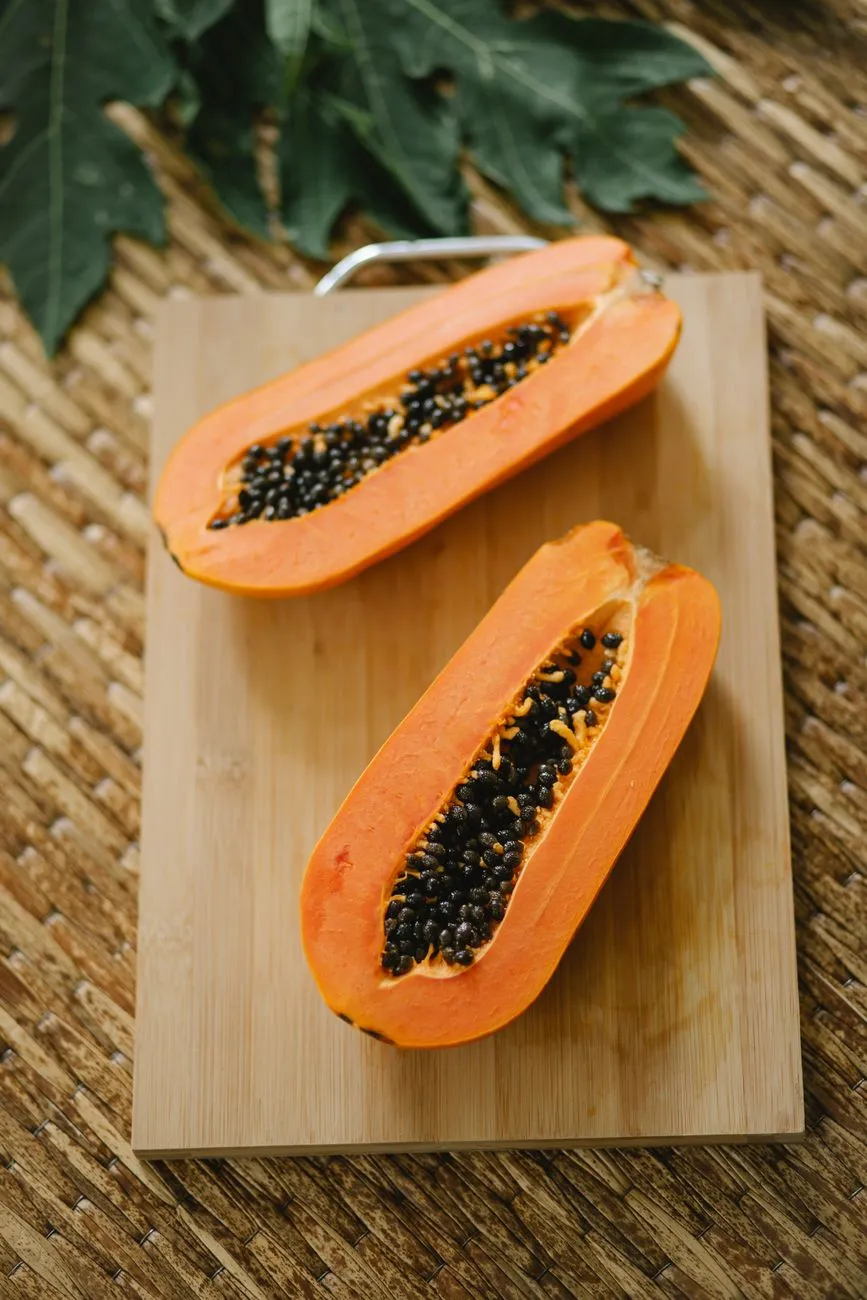 Person cutting papaya on a kitchen cutting board