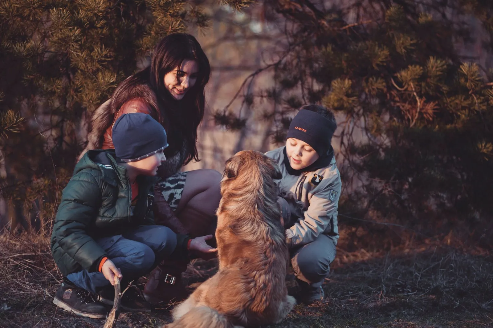 Family crouching beside a dog outdoors
