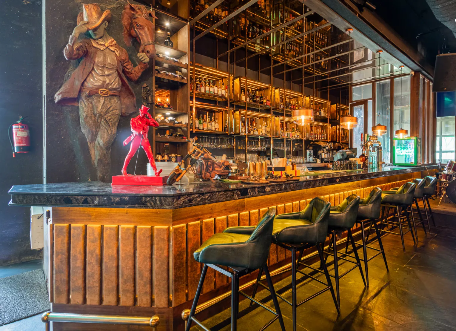 Bar counter with a cowboy wall sculpture, bottle shelves and green leather stools