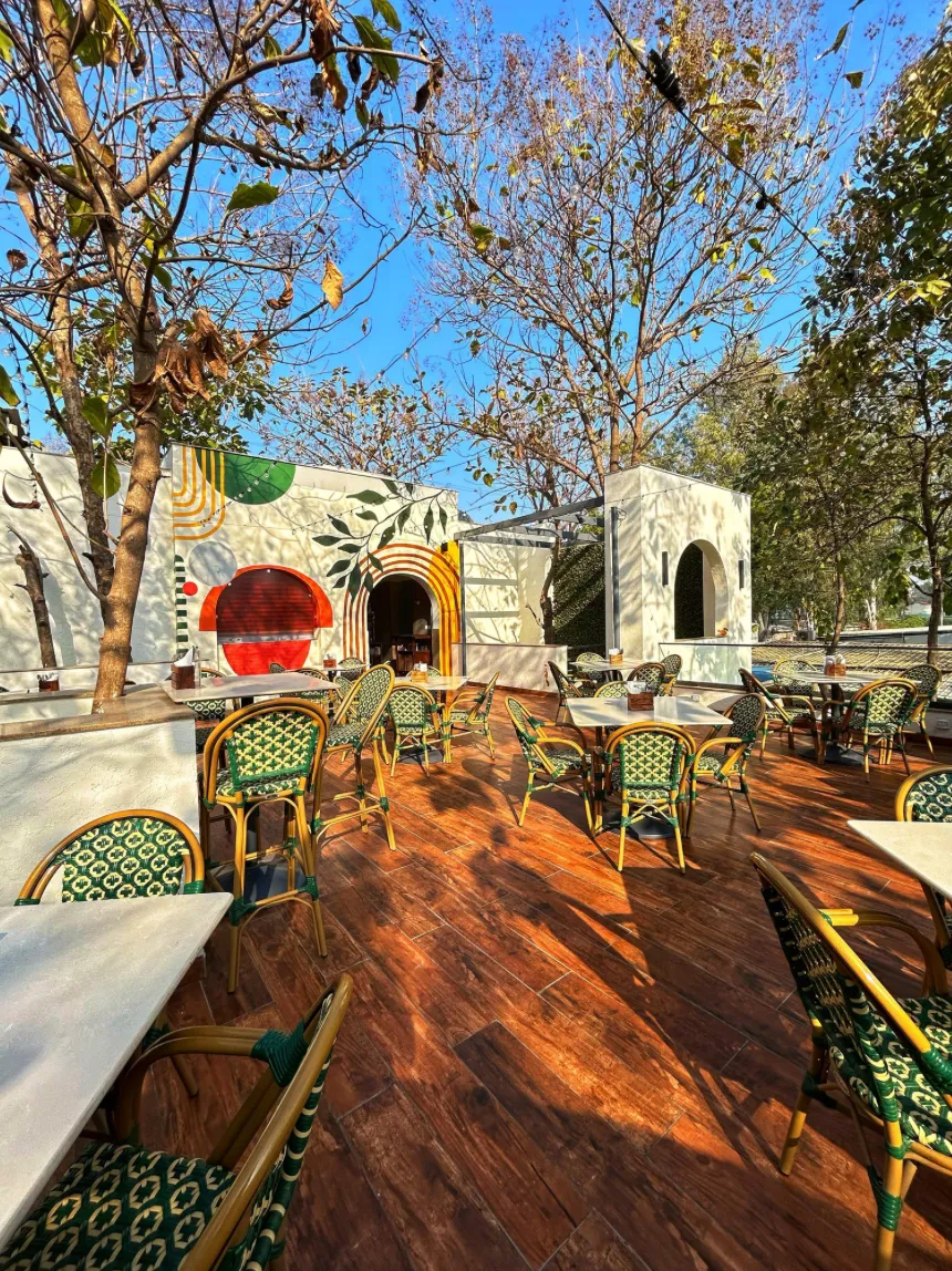 Outdoor cafe patio with rattan chairs, wooden deck flooring and leafy trees overhead
