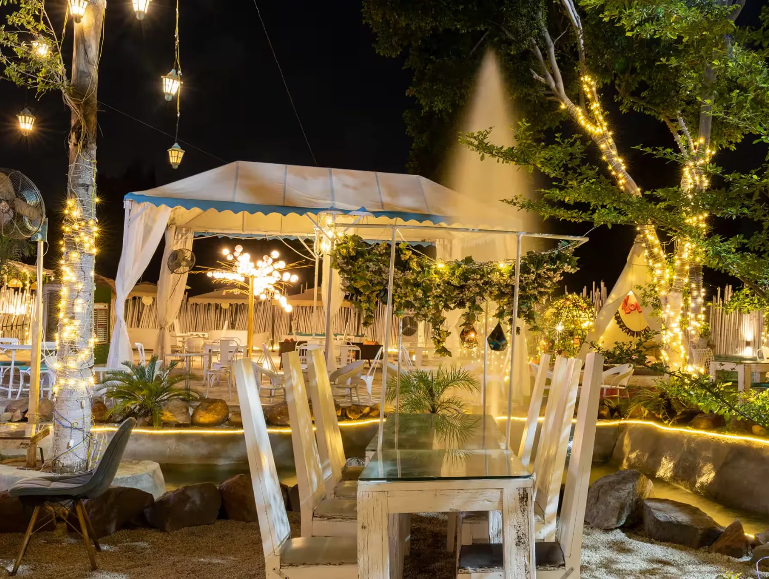 Outdoor cafe garden at night with string lights, a canopy tent and a wooden table