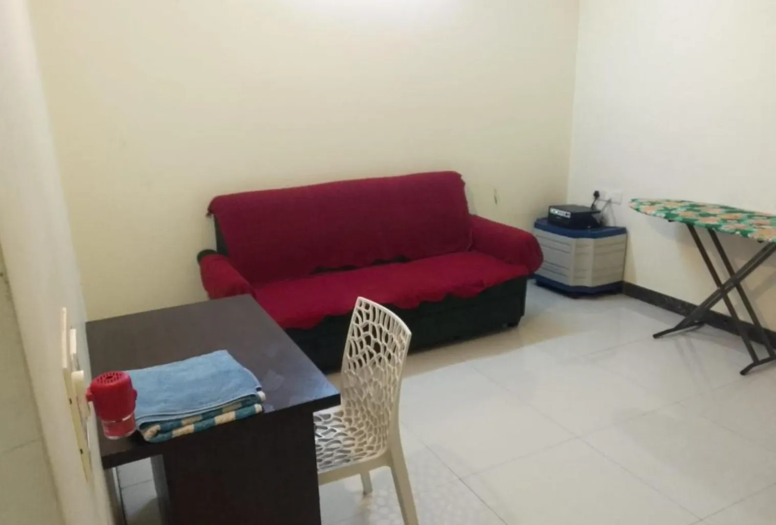 Simple room with a red sofa, desk, chair and ironing board on tiled floor