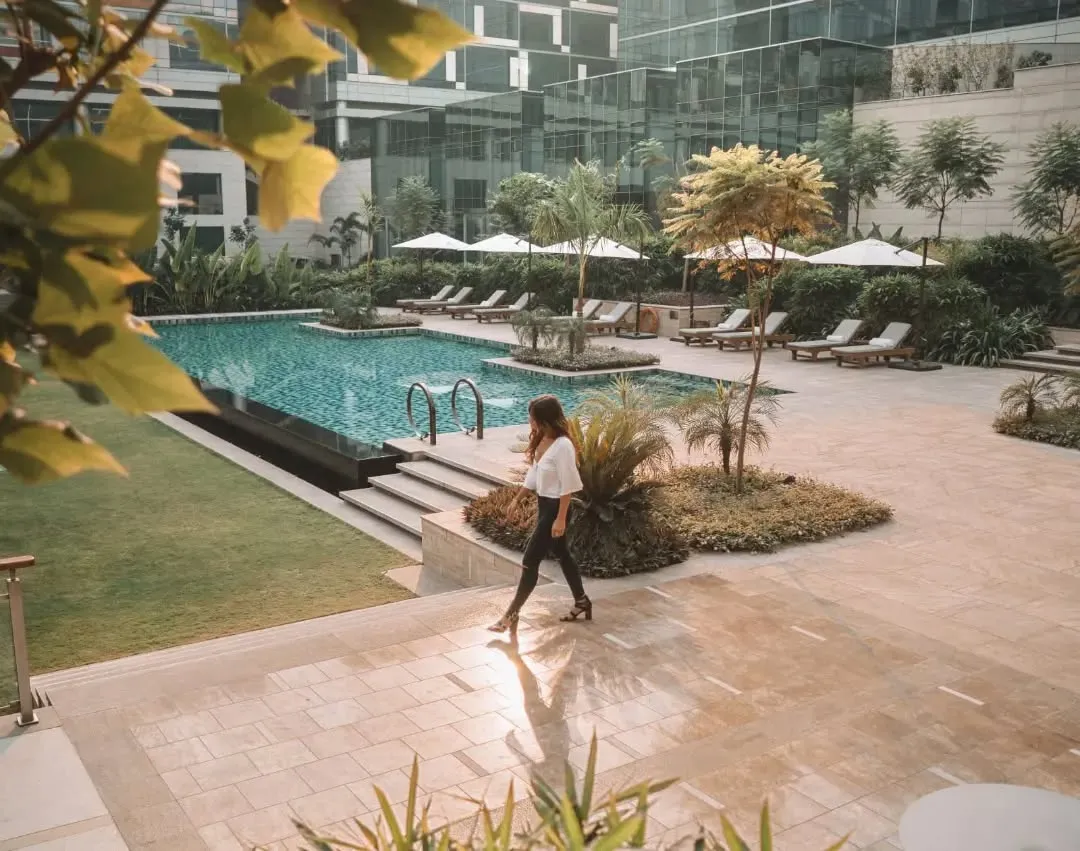 Woman walking beside an outdoor hotel pool with loungers and glass towers
