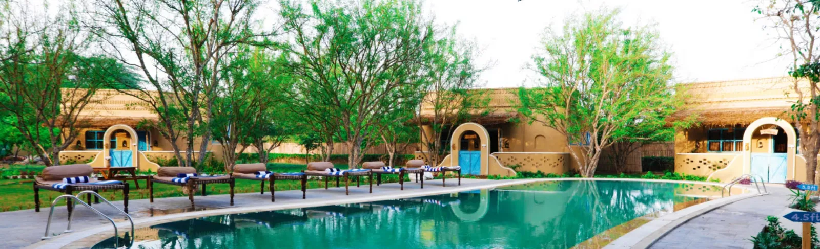 Poolside loungers beside mud-style cottages with blue doors and trees
