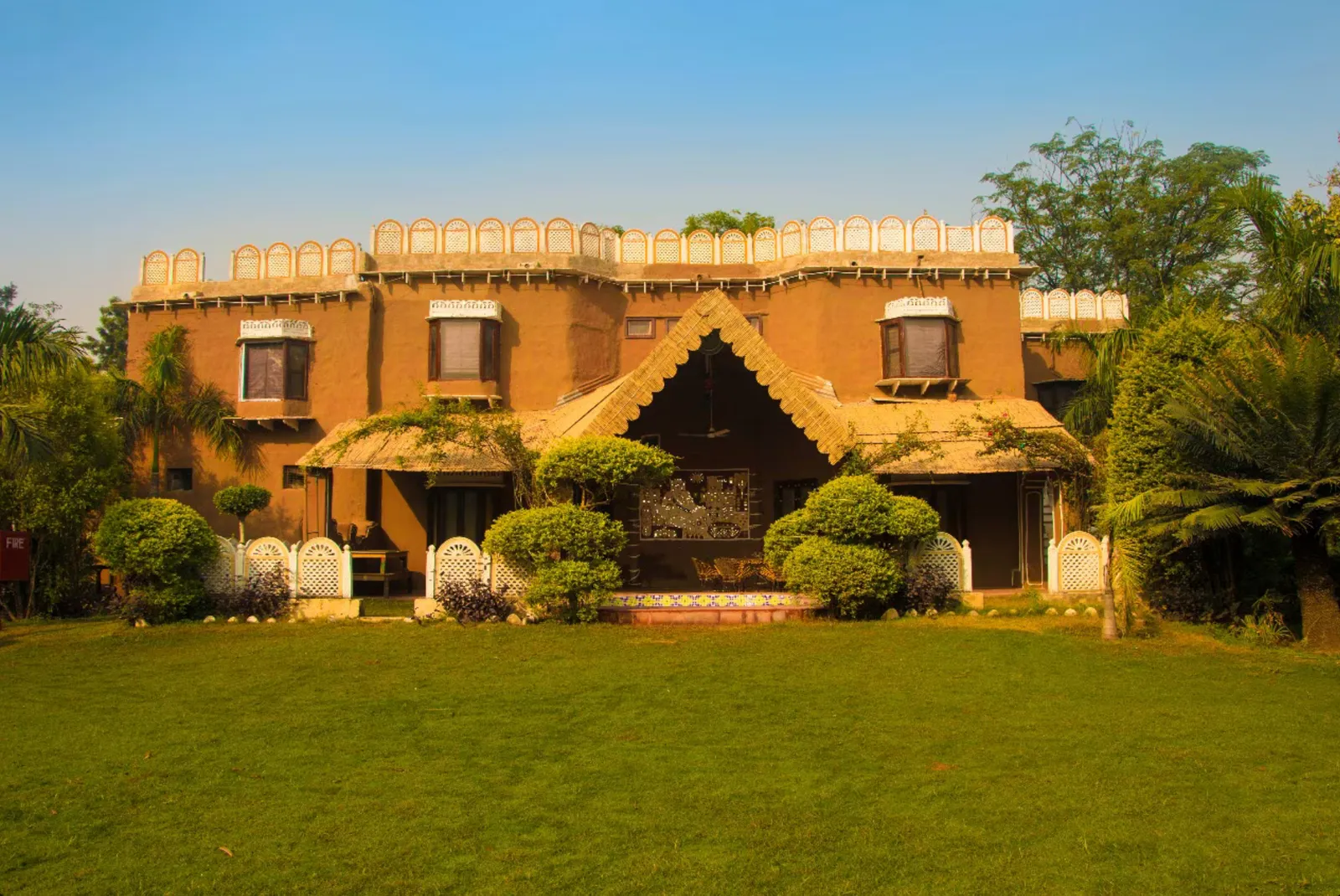 Traditional mud house resort with white lattice trim and a thatched roof porch