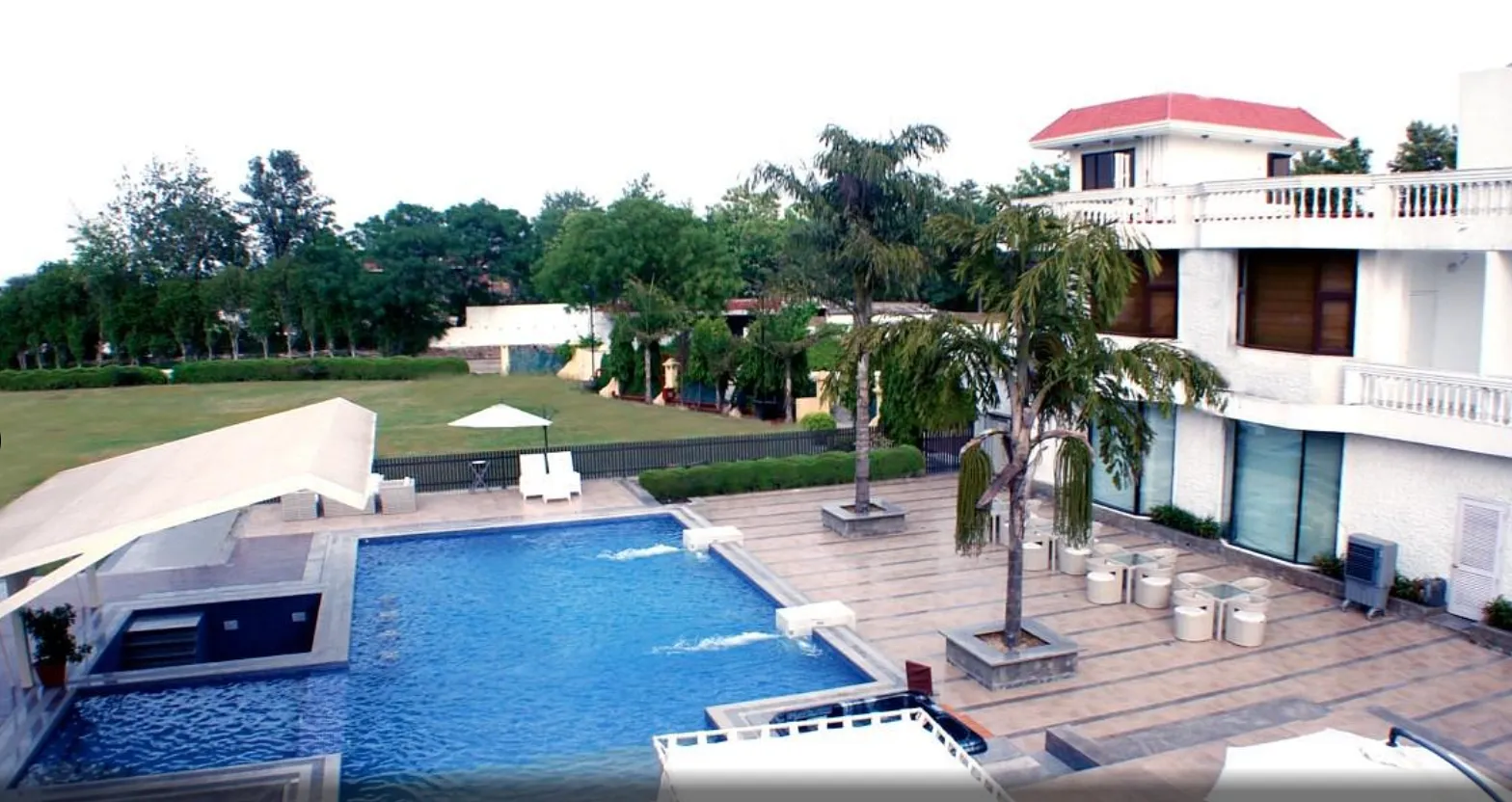 Rooftop pool view with palm trees and a white building topped by a red roof