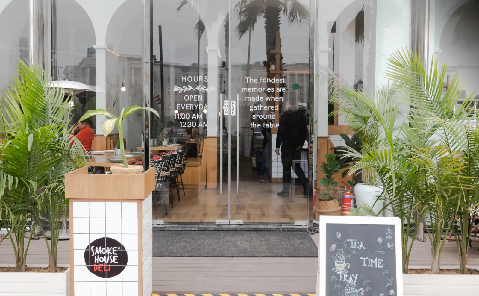 Smoke House Deli's glass storefront with potted palms and a chalkboard sign