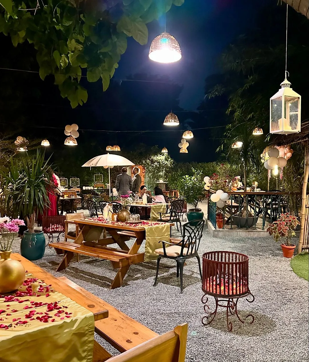 Outdoor tables scattered with rose petals under string lights at night