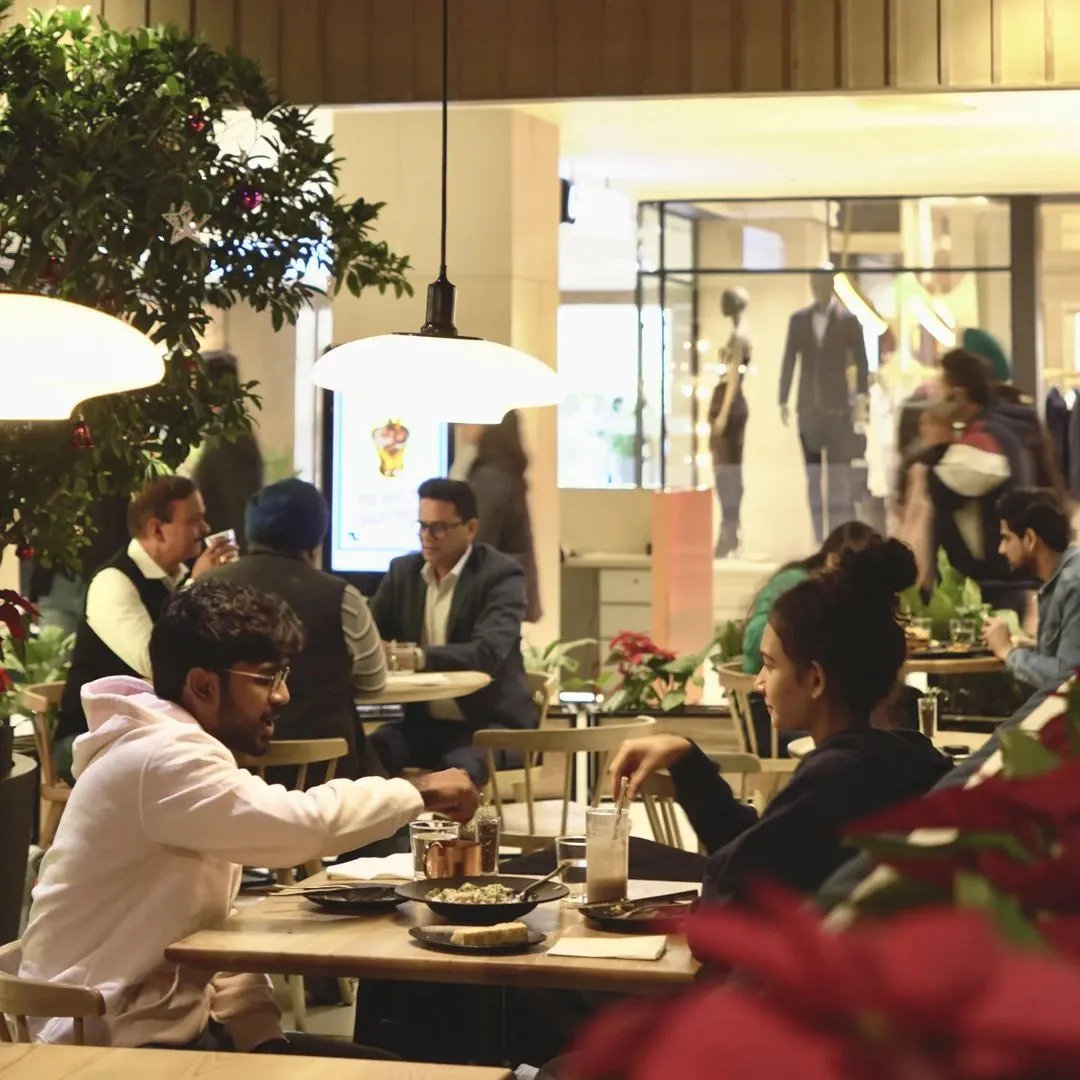 Two people chatting over drinks at a table inside a busy mall cafe