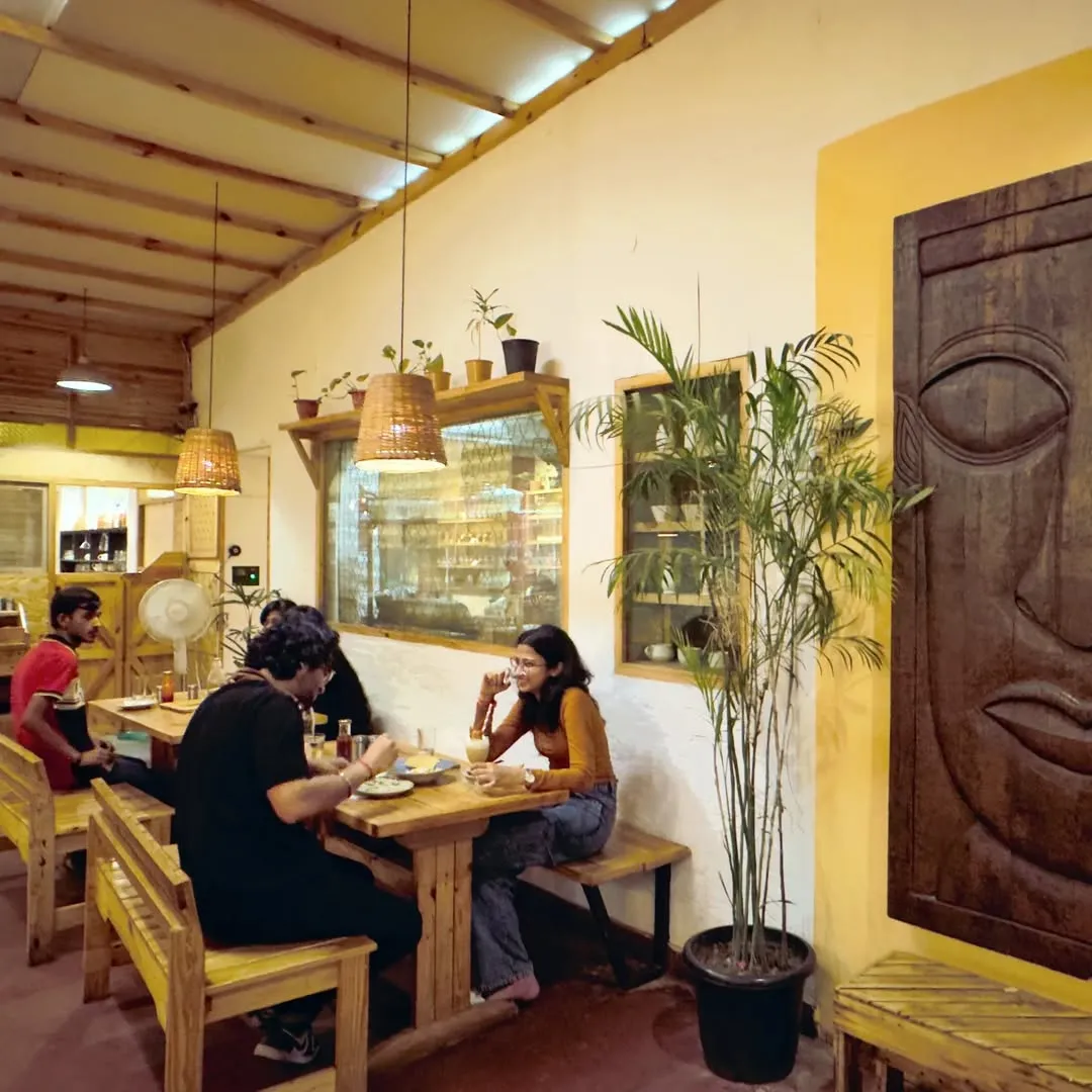 Customers seated at wooden bench tables inside a yellow-walled cafe