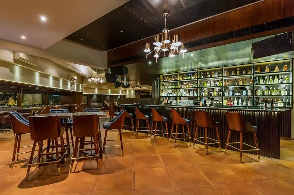 Dimly lit bar counter lined with bottles and leather bar stools