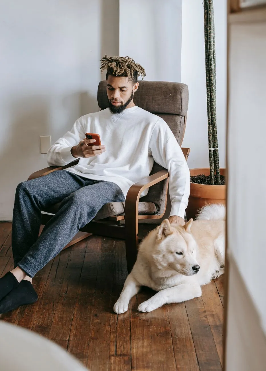 Person using a phone to manage pet care while sitting with a dog