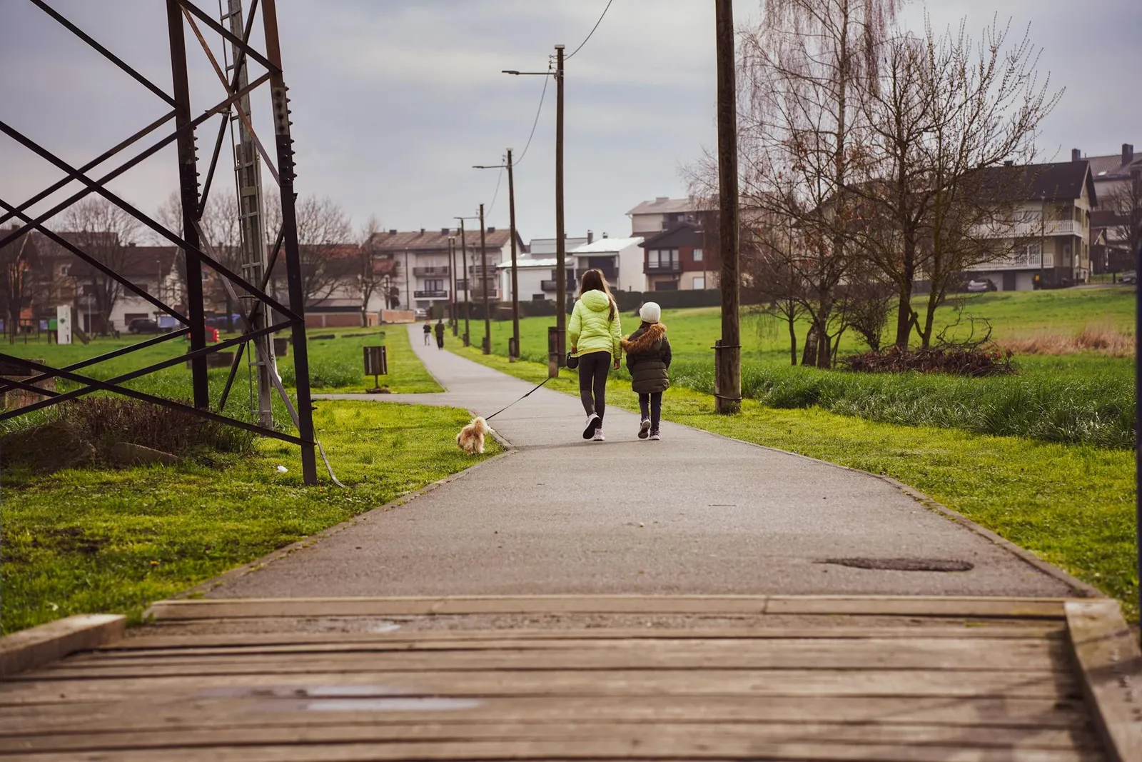 Two children walking a small dog on a leash along a paved path near houses