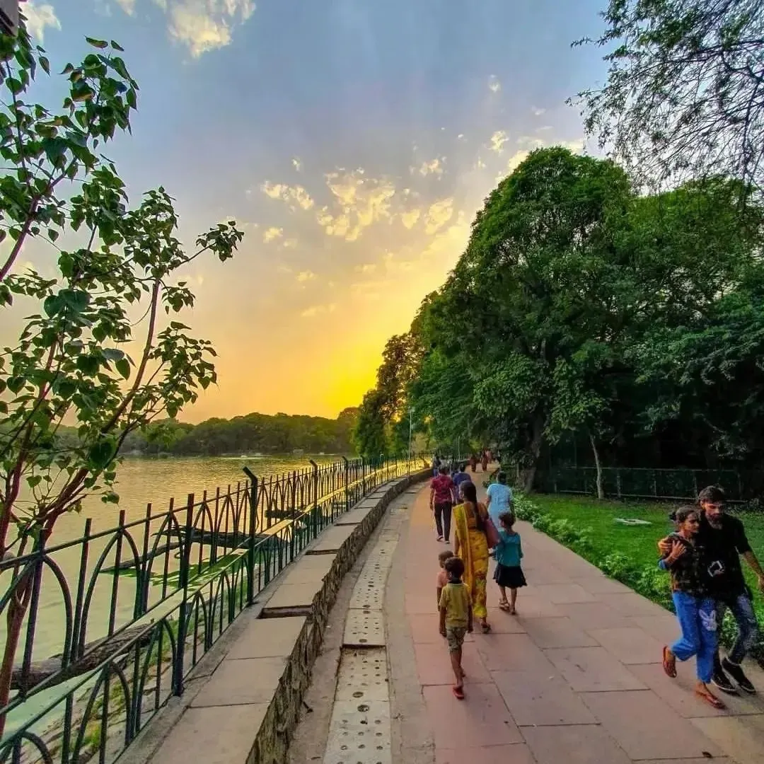 People walking along a tree-lined lakeside path at golden-hour sunset
