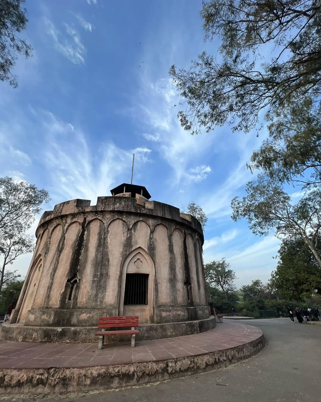 Round stone tower with a red bench beside it under a blue sky