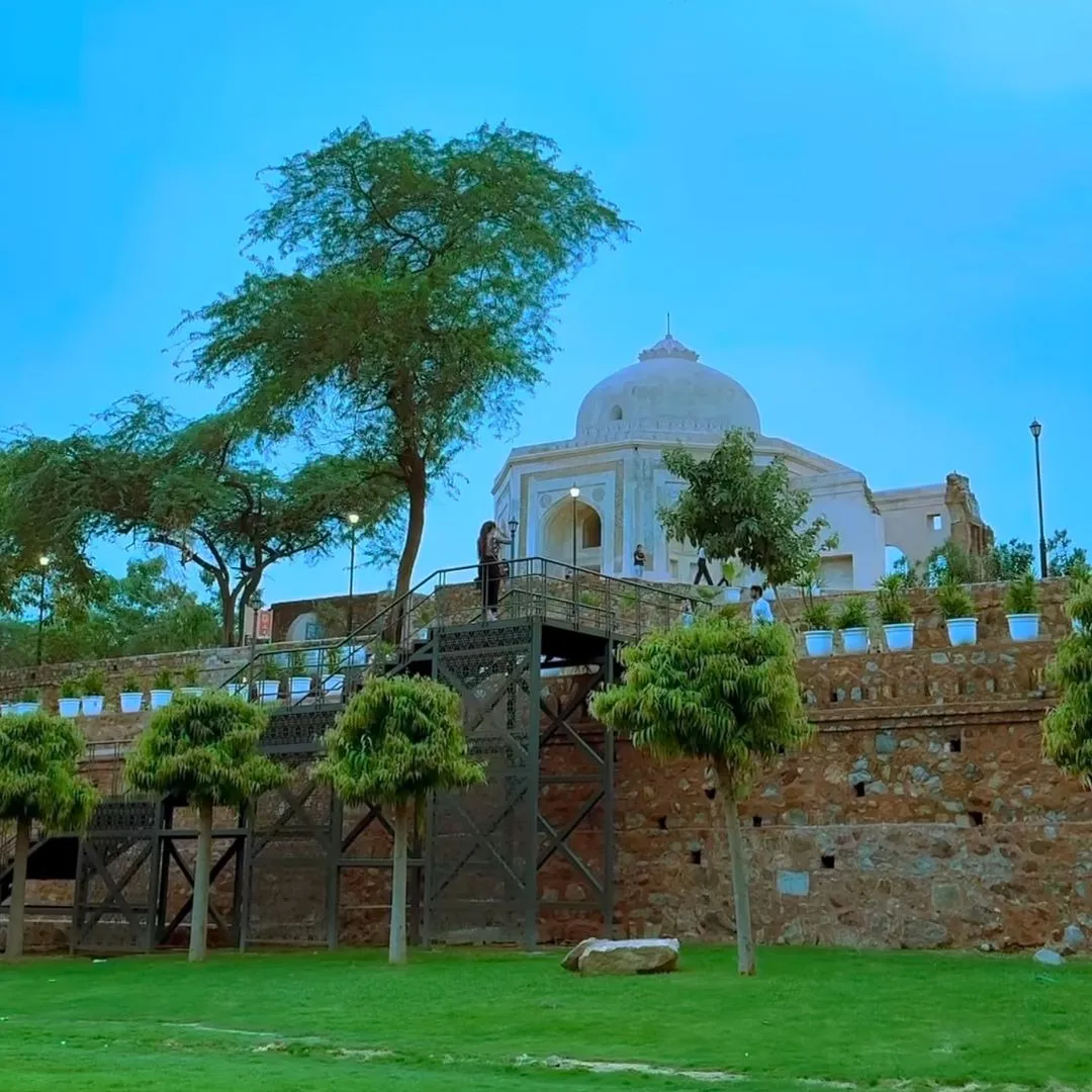 Domed heritage monument atop a stone wall surrounded by trees and a lawn